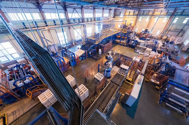 High angle full length portrait of bearded businessman wearing hardhat walking across production workshop accompanied by female factory employee