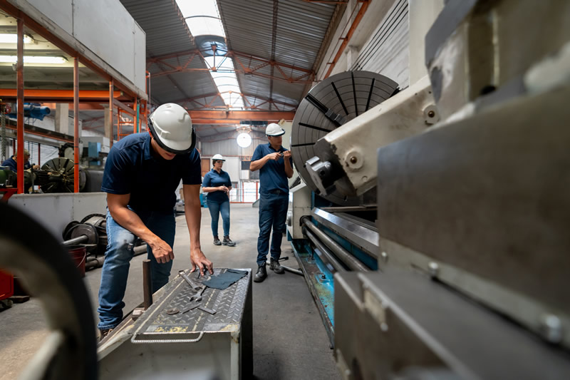 men working at a metallurgy factory using a machine and wearing protective wear